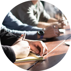 A picture of people in a meeting, with someone taking notes.